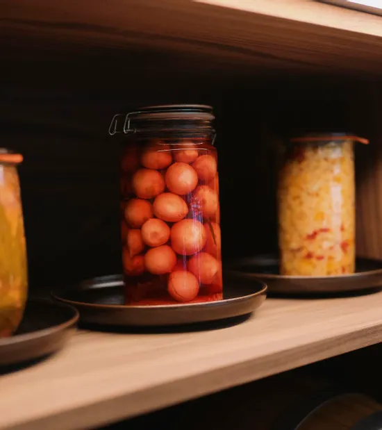 Glass jars of homemade pickled vegetables and preserved tomatoes on a wooden shelf